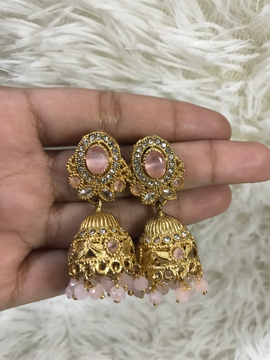 Gold and pink earrings held in a hand against a white fur background