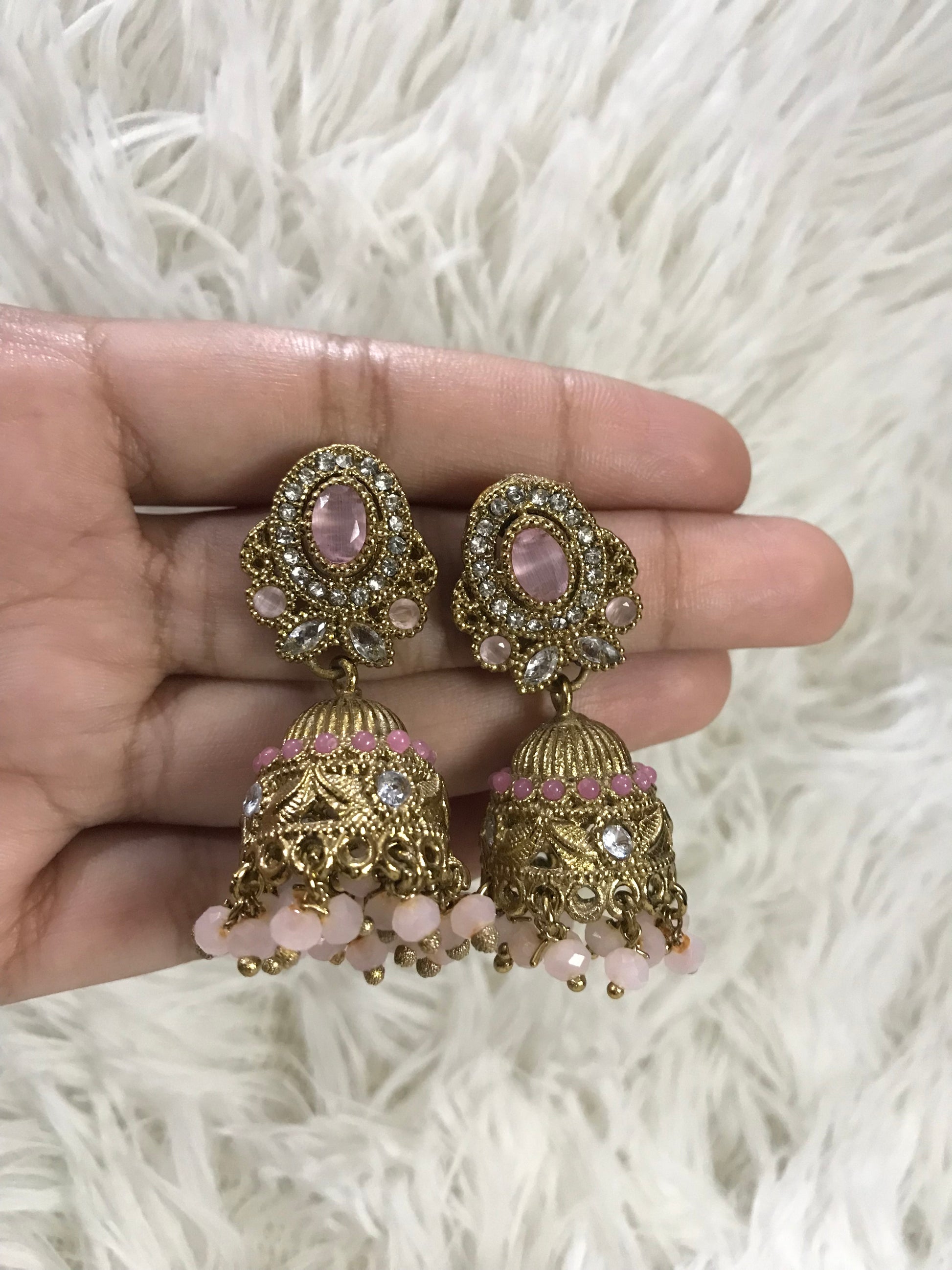 Gold and pink decorative earrings held in a hand on a white fluffy background