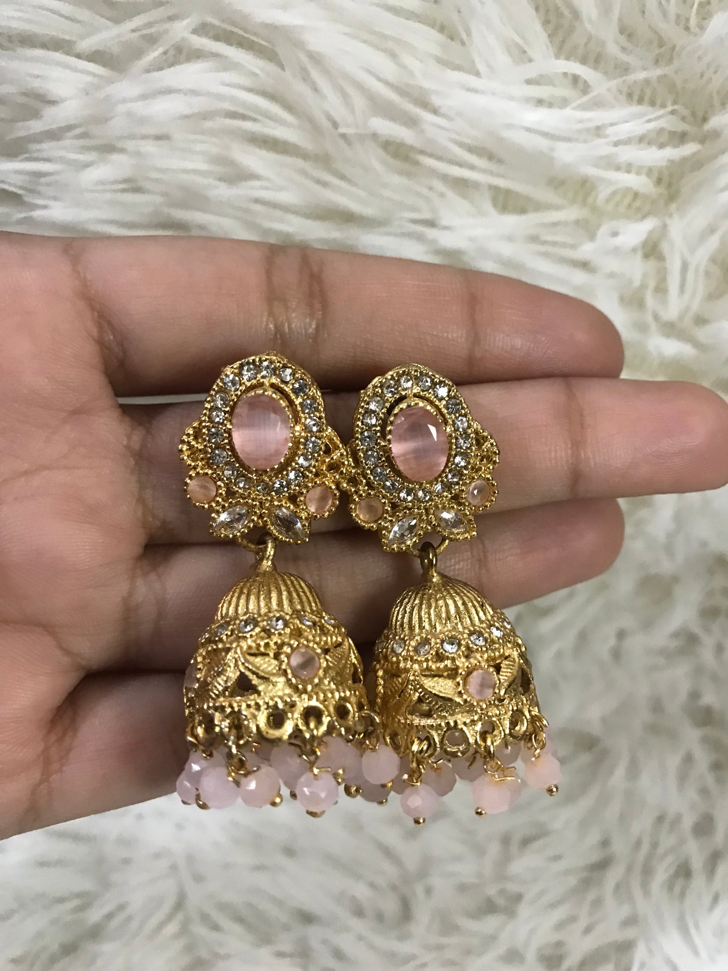 Gold and pink earrings held in a hand against a white fur background