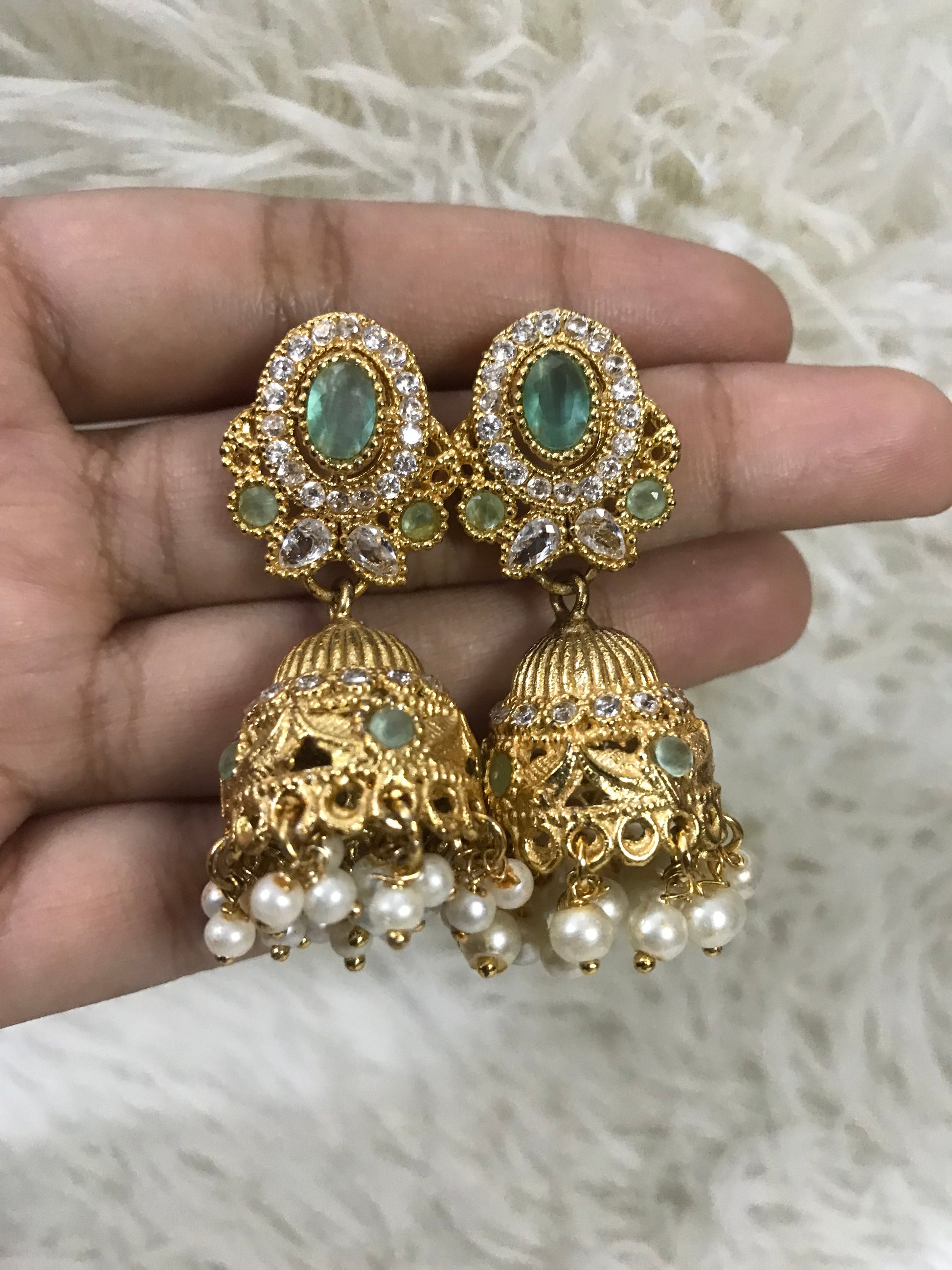 Gold and pearl earrings held in a hand against a white fur background